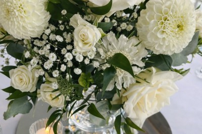 Table élégamment dressée avec nappes blanches, serviettes pliées, verres et décorations florales dans une salle lumineuse.