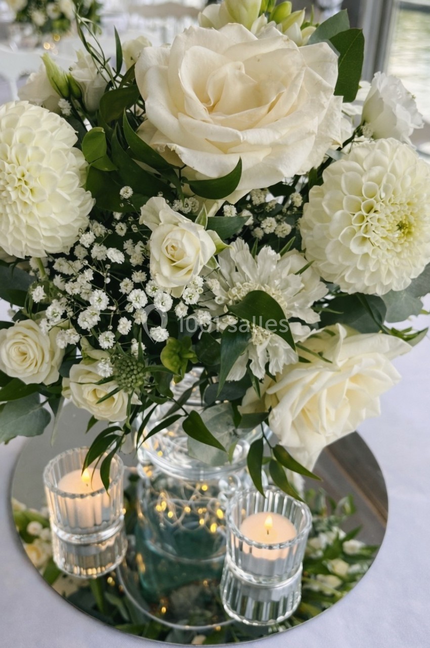 Bouquet de fleurs blanches avec roses, dahlias et gypsophiles, posé sur un miroir avec deux bougies allumées.