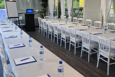 Table élégamment dressée avec nappes blanches, serviettes pliées, verres et décorations florales dans une salle lumineuse.
