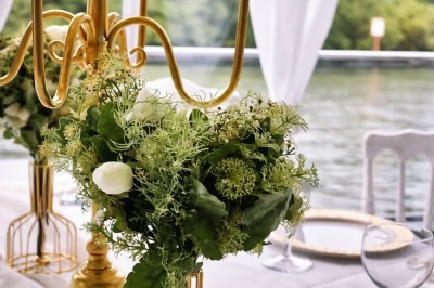 Table élégamment dressée avec nappes blanches, serviettes pliées, verres et décorations florales dans une salle lumineuse.