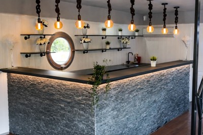 Table élégamment dressée avec nappes blanches, serviettes pliées, verres et décorations florales dans une salle lumineuse.