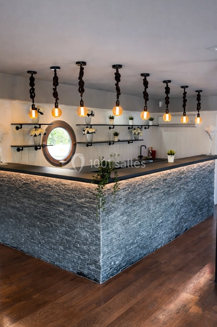 Comptoir en pierre grise avec étagères murales noires, suspensions lumineuses et décoration végétale.