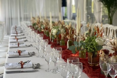 Table élégamment dressée avec nappes blanches, serviettes pliées, verres et décorations florales dans une salle lumineuse.