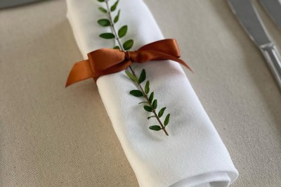 Table élégamment dressée avec nappes blanches, serviettes pliées, verres et décorations florales dans une salle lumineuse.
