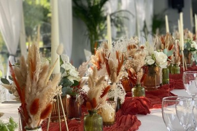 Table élégamment dressée avec nappes blanches, serviettes pliées, verres et décorations florales dans une salle lumineuse.