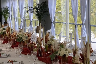 Table élégamment dressée avec nappes blanches, serviettes pliées, verres et décorations florales dans une salle lumineuse.
