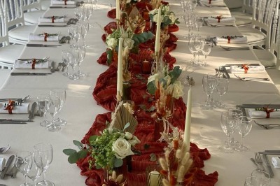 Table élégamment dressée avec nappes blanches, serviettes pliées, verres et décorations florales dans une salle lumineuse.