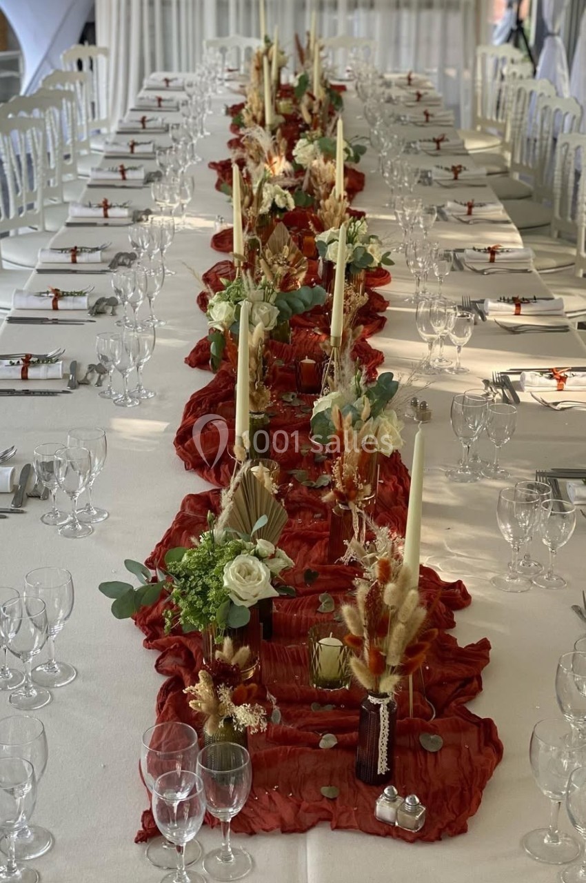 Table décorée pour un événement avec nappes blanches, chemin de table rouge, bougies et compositions florales.