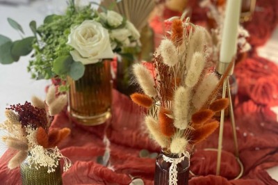 Table élégamment dressée avec nappes blanches, serviettes pliées, verres et décorations florales dans une salle lumineuse.