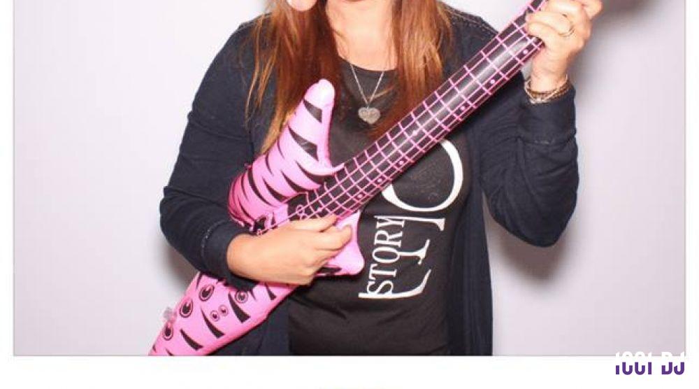 Femme tenant une guitare gonflable rose avec un motif zébré, posant devant un fond clair.