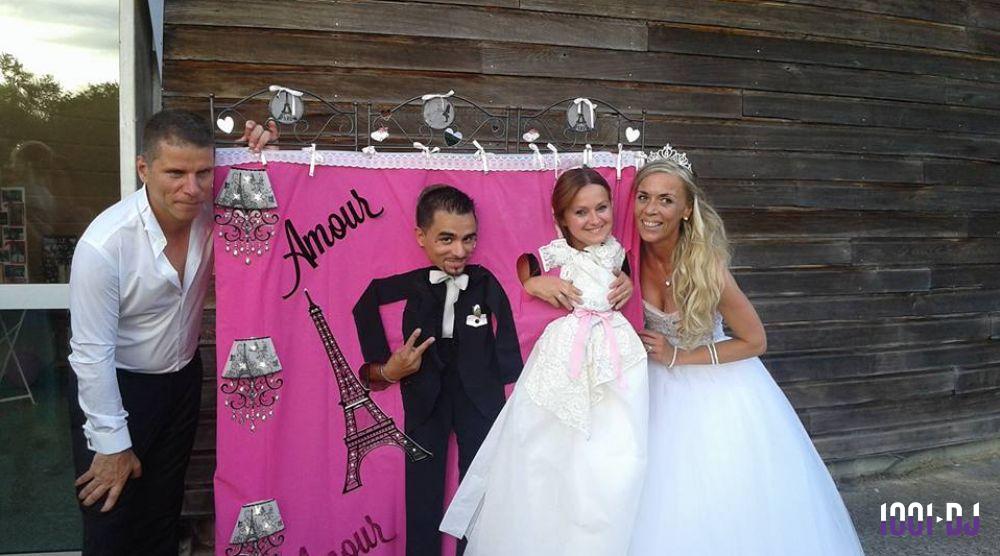 Un groupe de personnes pose devant un décor rose avec des motifs de mariage et une Tour Eiffel stylisée.