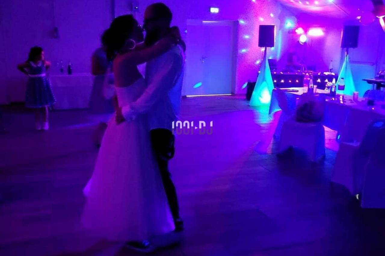 Un couple danse dans une salle faiblement éclairée avec des lumières colorées et une ambiance festive.