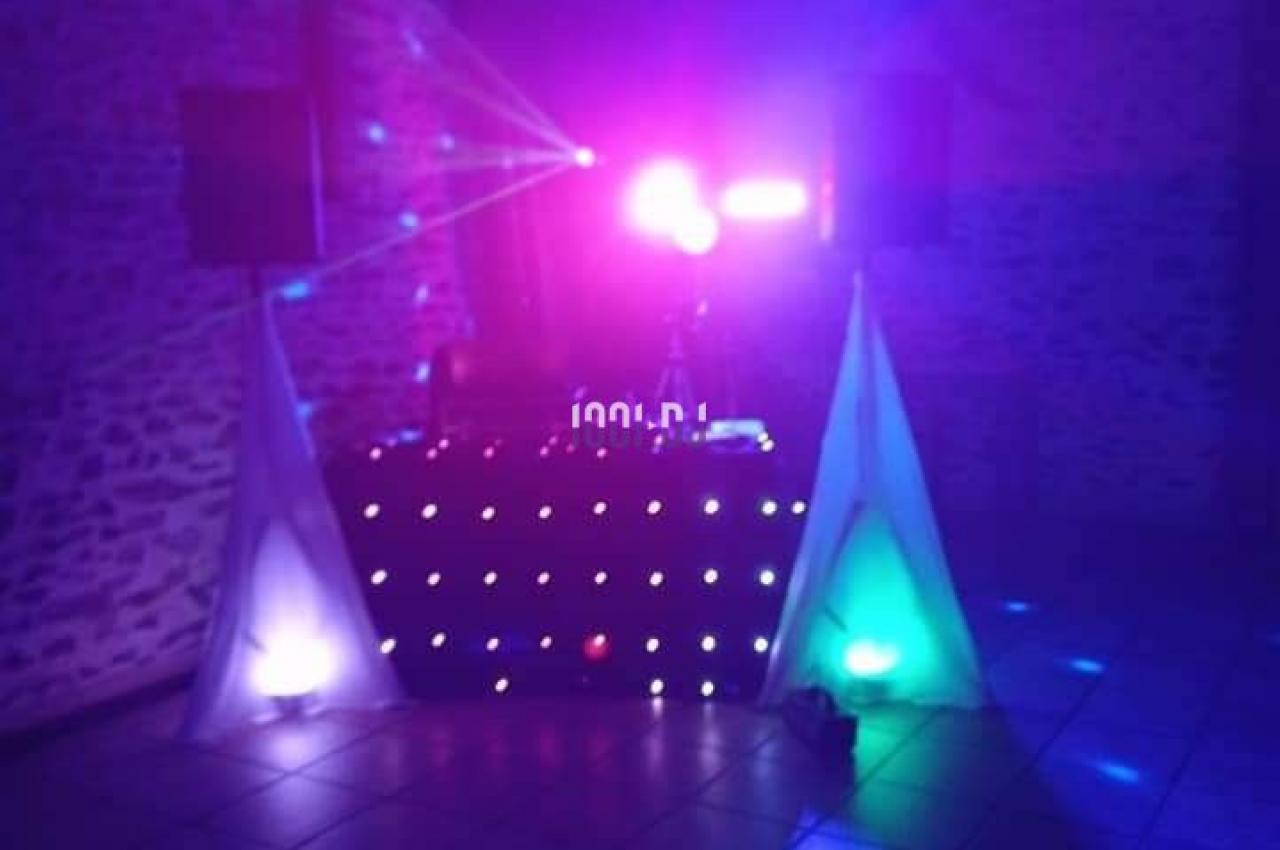 Installation de DJ avec jeux de lumières colorées dans une salle aux murs en pierre et au sol carrelé.