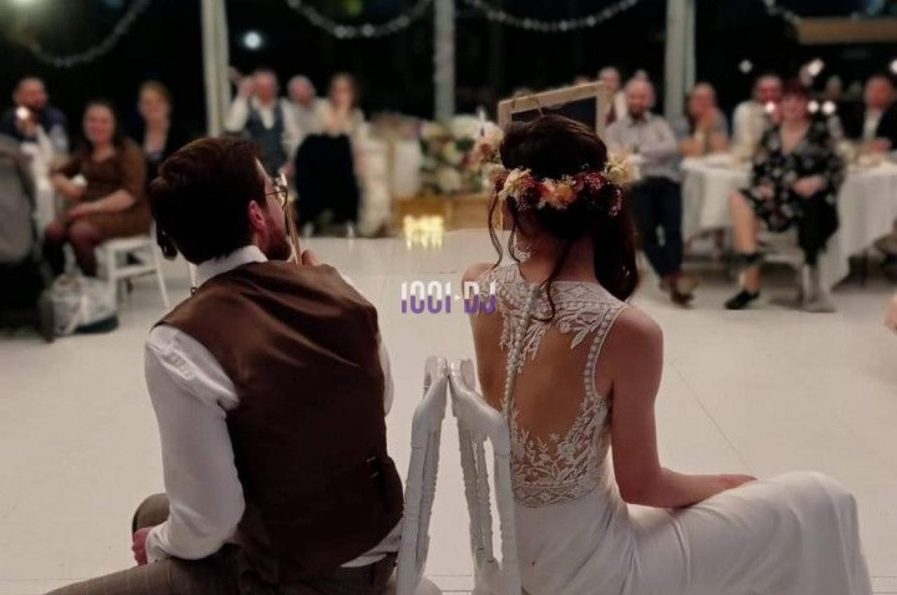 Un couple assis dos à dos sur des chaises lors d'une réception de mariage dans une salle lumineuse.