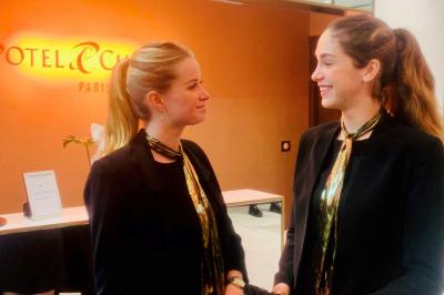 Femme souriante portant un béret rouge, debout près d'une vitrine décorée de fleurs colorées et de montres exposées.