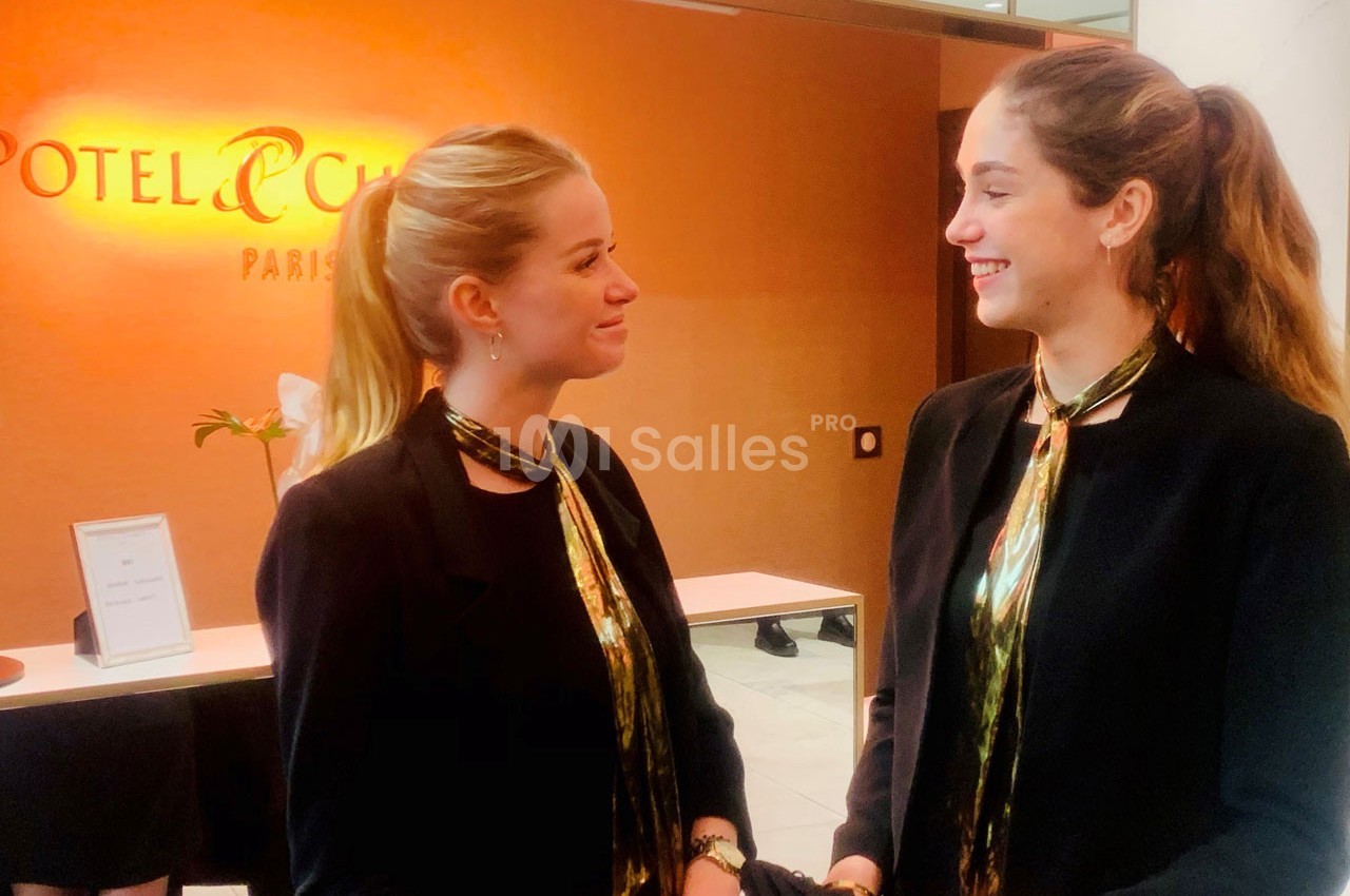 Deux hôtesses en uniforme noir discutent devant un comptoir d'accueil dans un hôtel à Paris.