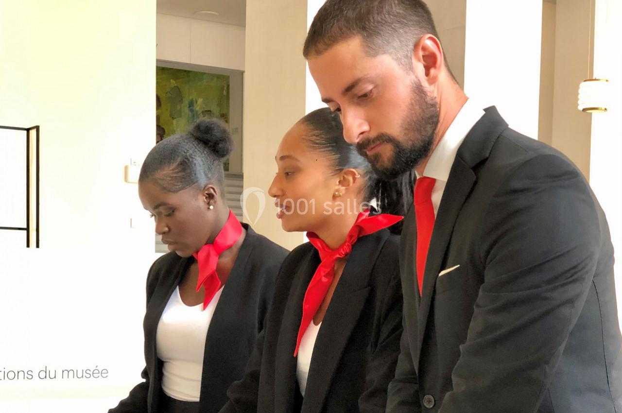 Trois personnes en tenue professionnelle avec foulards rouges discutent dans un environnement lumineux.