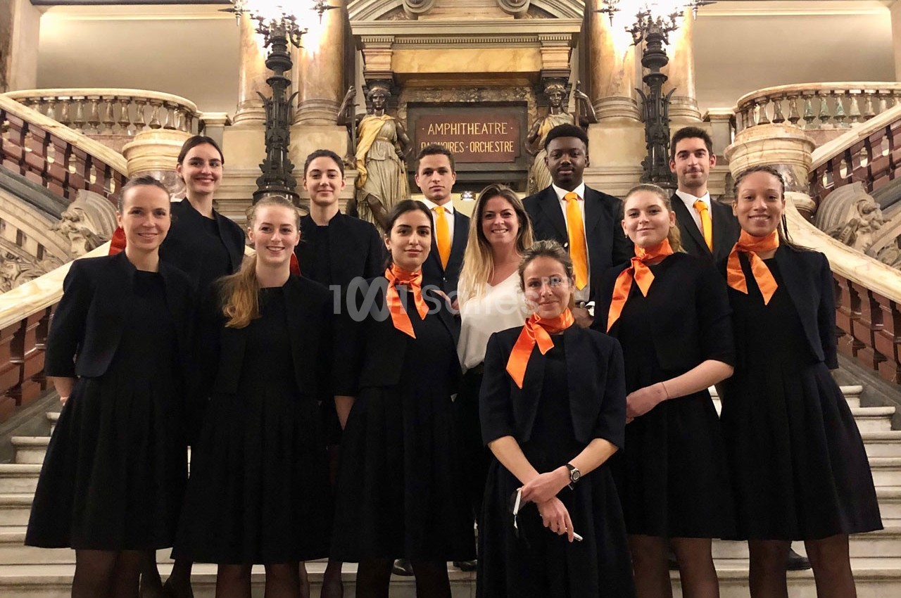Un groupe de personnes en tenue formelle posant sur un escalier intérieur devant une architecture ornée.