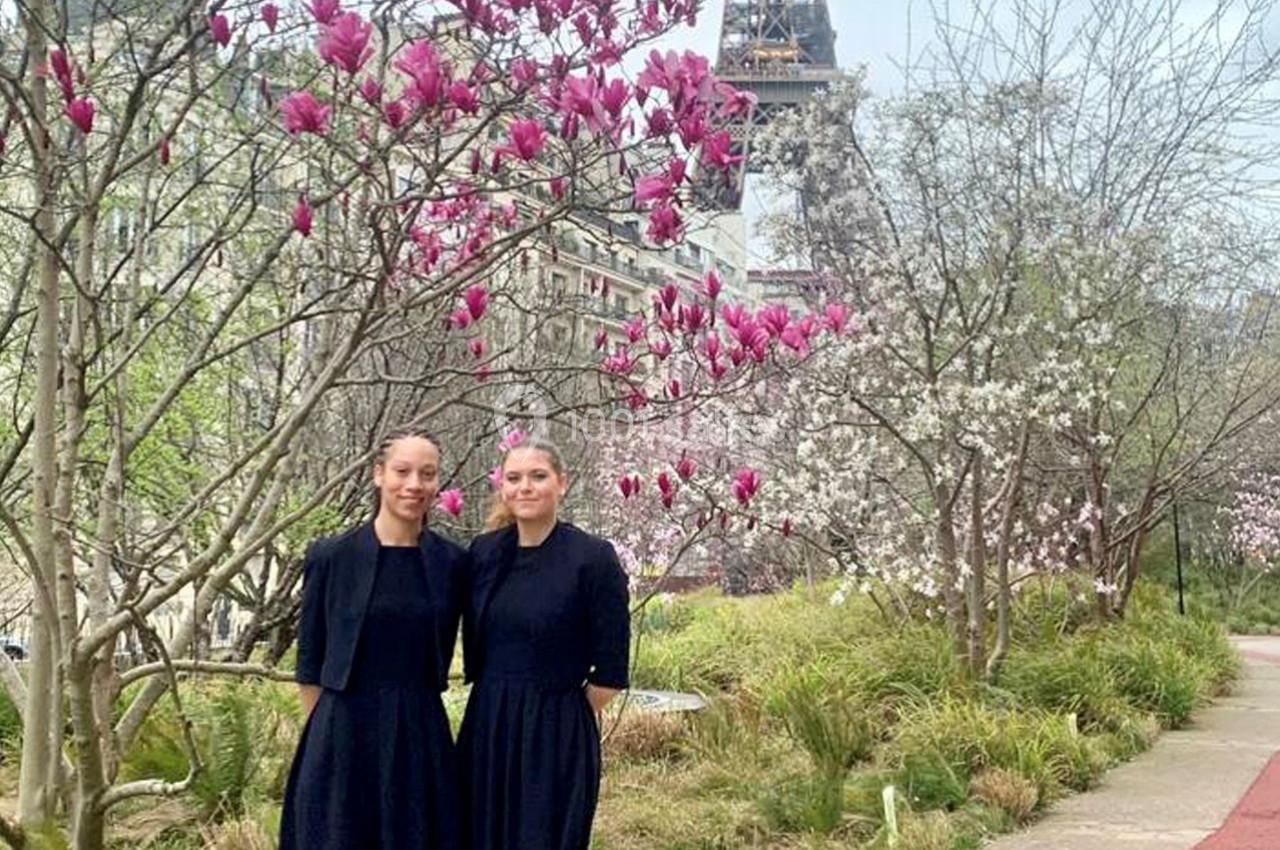 Deux femmes en tenue noire posent devant des magnolias en fleurs, avec la tour Eiffel en arrière-plan.