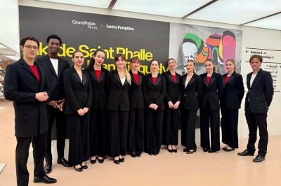 Miniature MHBA - Mon Hôte-sse Bien Aimé-e #5 Quatre femmes en robe noire sourient debout sur une terrasse en bois avec un fond de verdure.