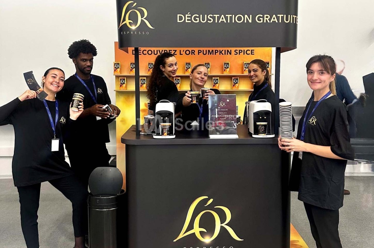 Équipe souriante devant un stand proposant une dégustation gratuite de café avec machines et gobelets exposés.