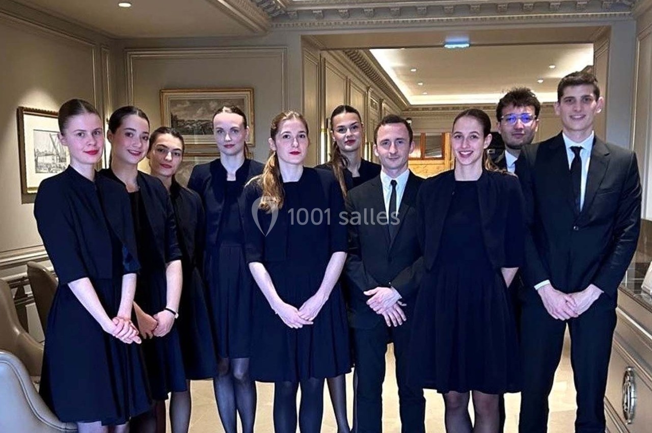 Photo MHBA - Mon Hôte-sse Bien Aimé-e #9 Un groupe de personnes en tenue formelle posant dans un intérieur élégant avec des murs ornés de cadres.