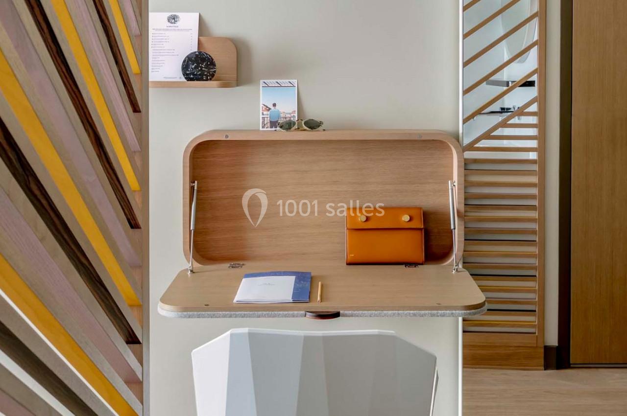 Bureau mural en bois clair avec une pochette orange, un carnet, un crayon et des éléments décoratifs en arrière-plan.