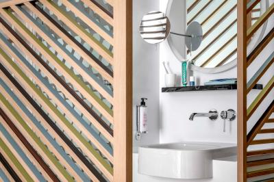 Lavabo moderne avec miroir rond, étagère murale, robinet chromé et panneaux en bois ajourés en premier plan.