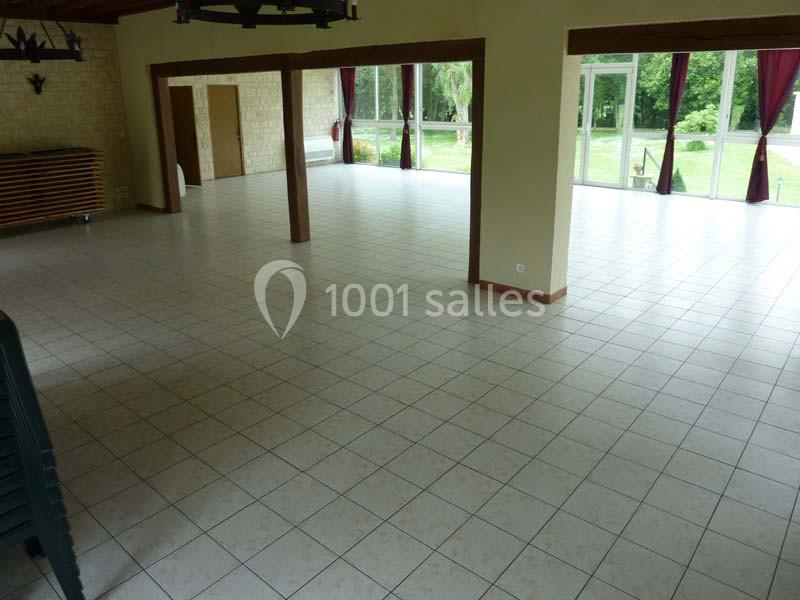 Salle spacieuse avec carrelage clair, grandes baies vitrées et vue sur un espace vert extérieur.