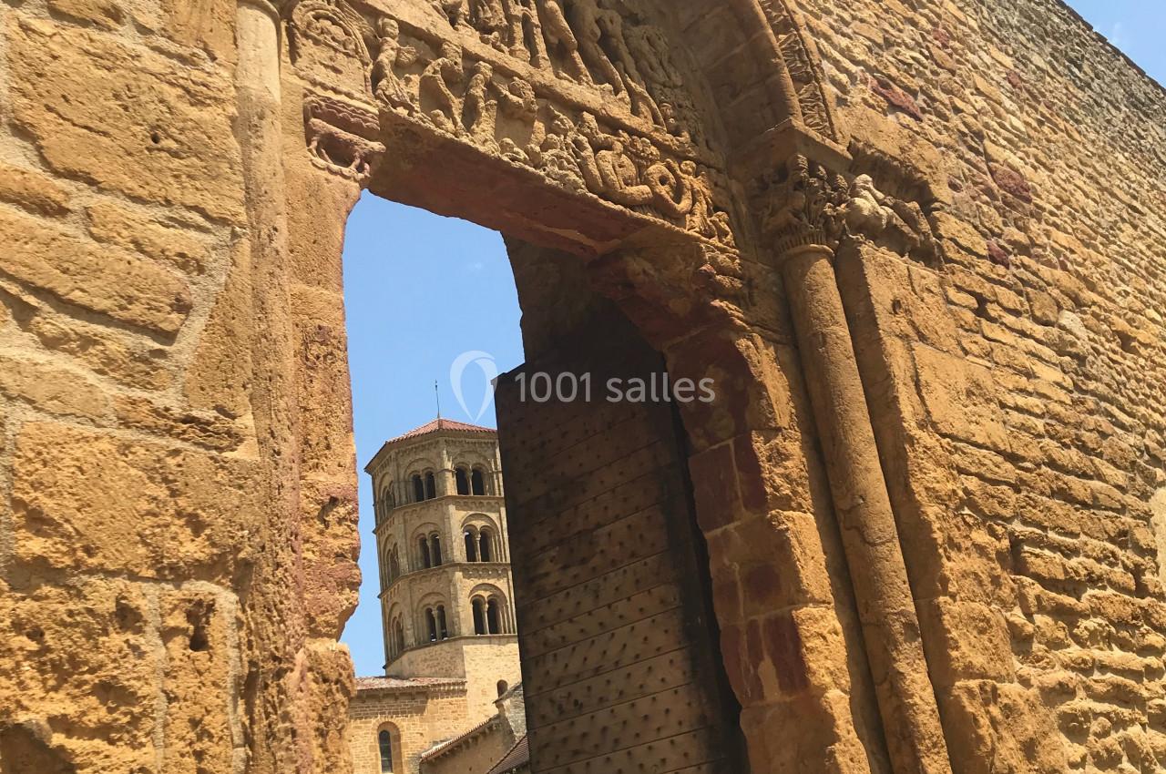 Vue d'une porte en pierre sculptée donnant sur une tour romane sous un ciel bleu.
