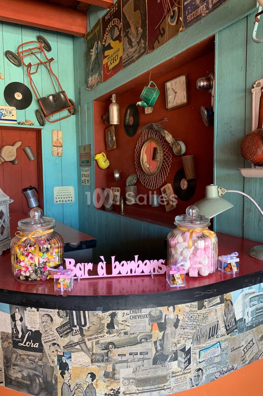 Bar à bonbons rétro avec pots remplis de sucreries colorées, décor vintage avec affiches et objets anciens.