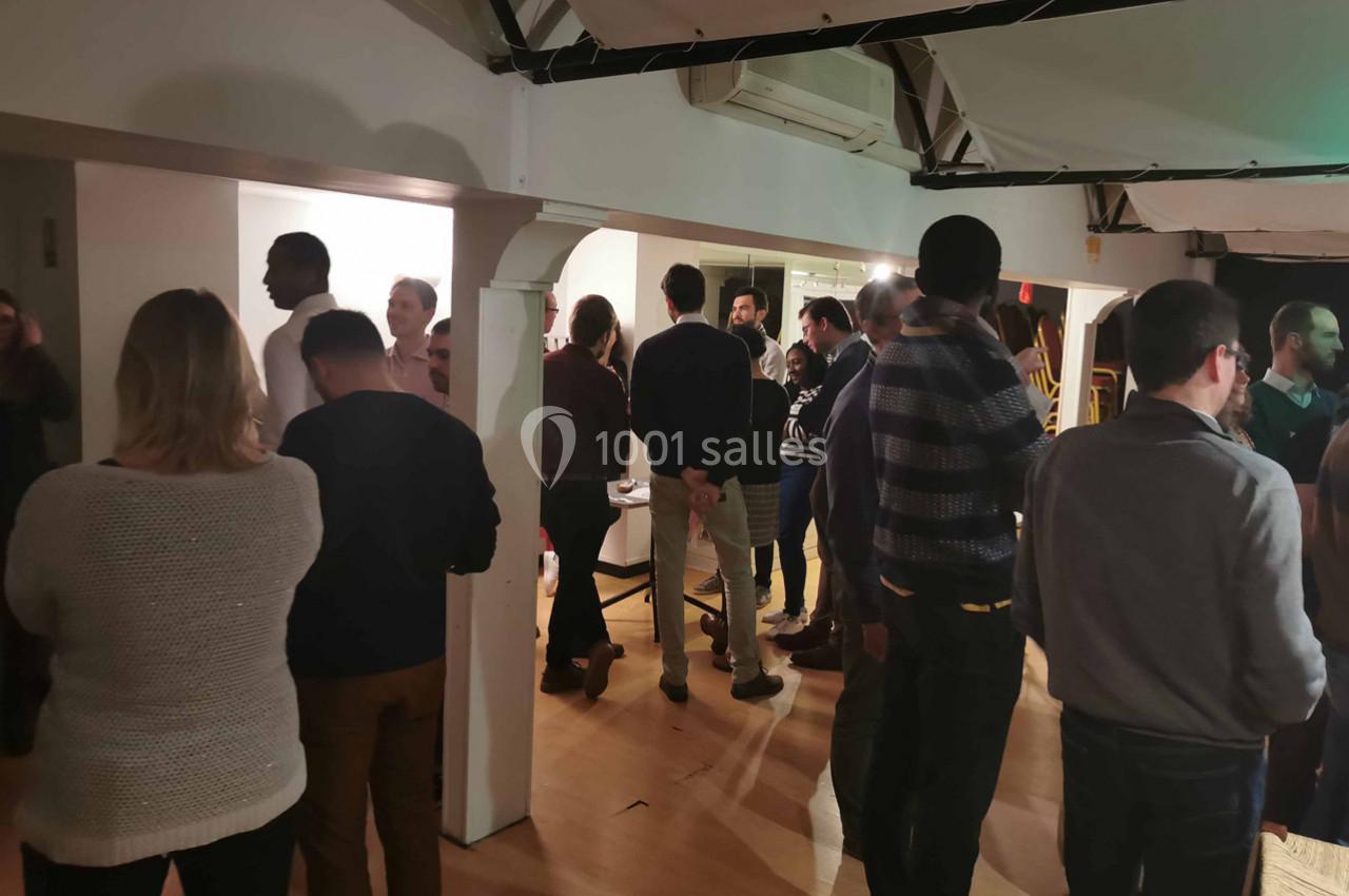 Groupe de personnes discutant dans une salle éclairée, avec des poutres apparentes et un sol en bois.