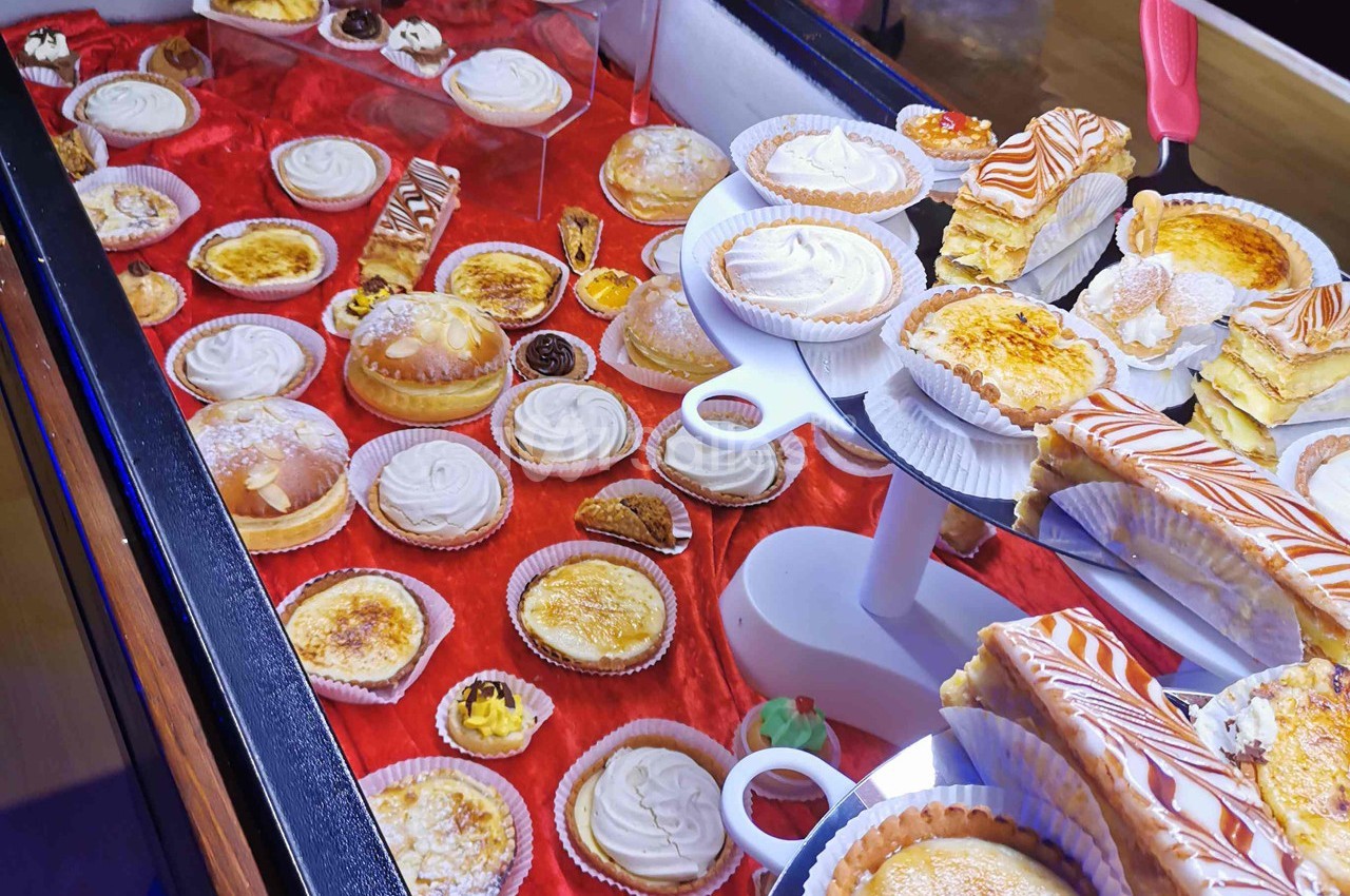 Vitrine présentant une variété de pâtisseries sur un fond rouge, incluant tartes, éclairs et gâteaux individuels.