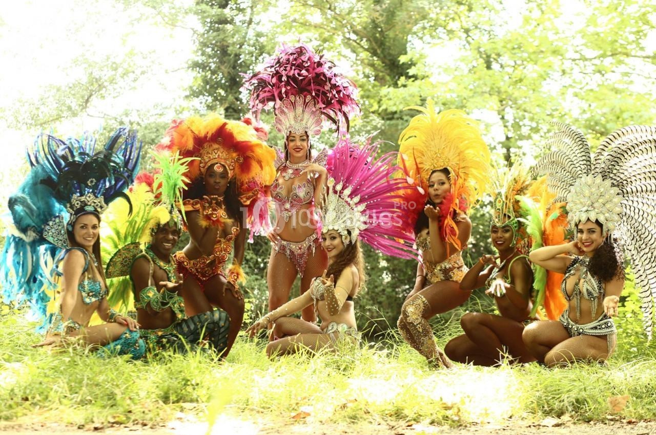 Un groupe de danseuses en costumes colorés et ornés de plumes posant dans un cadre naturel verdoyant.