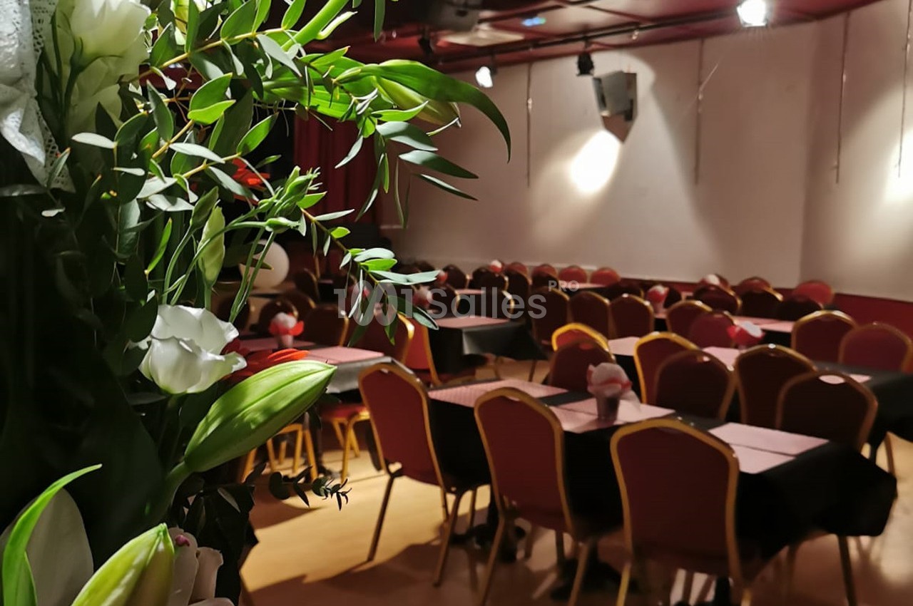 Salle de réception avec des chaises alignées et des tables dressées, décorée de fleurs au premier plan.