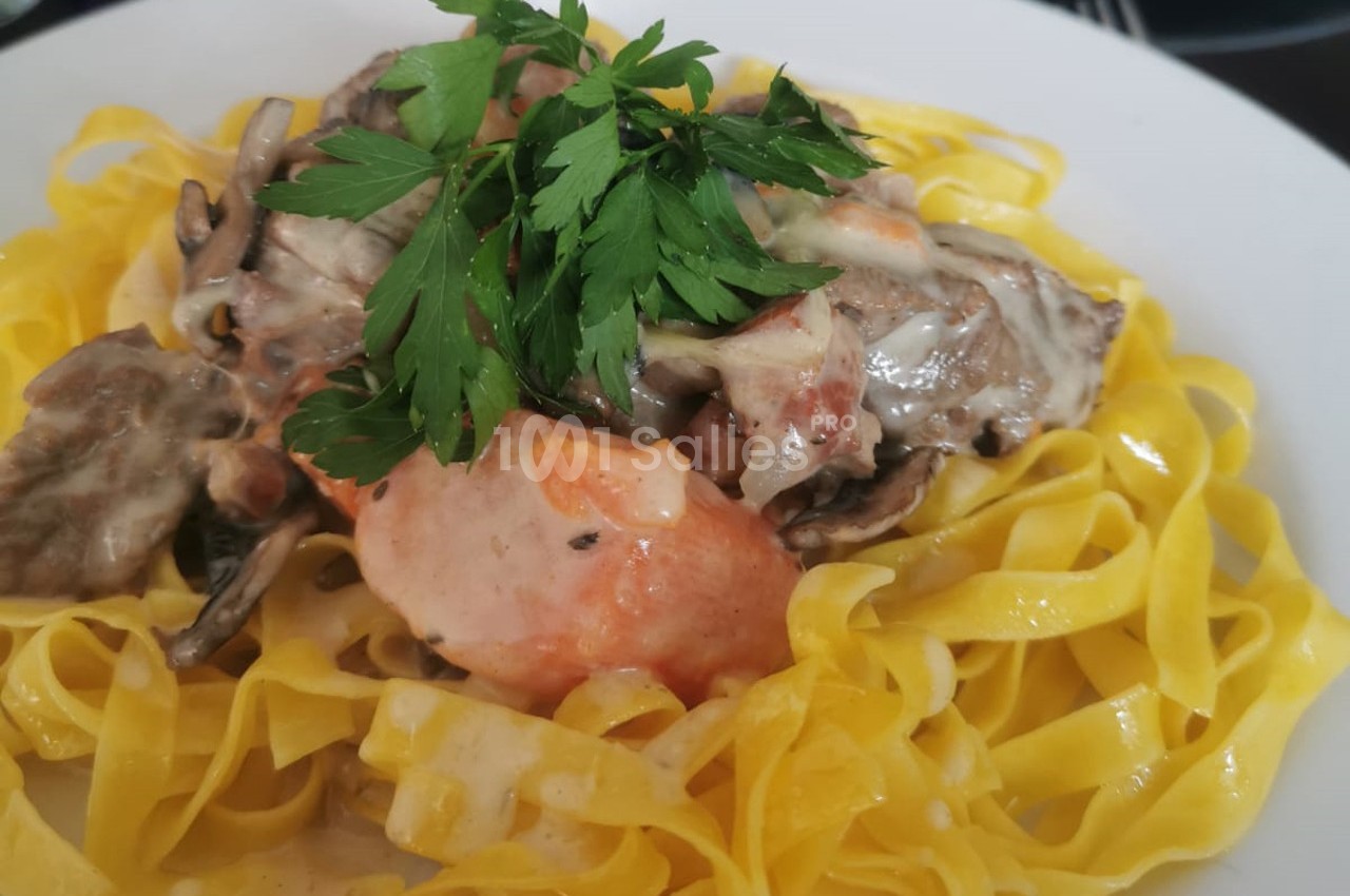 Assiette de tagliatelles fraîches garnies de sauce crémeuse aux champignons et décorée de persil frais.