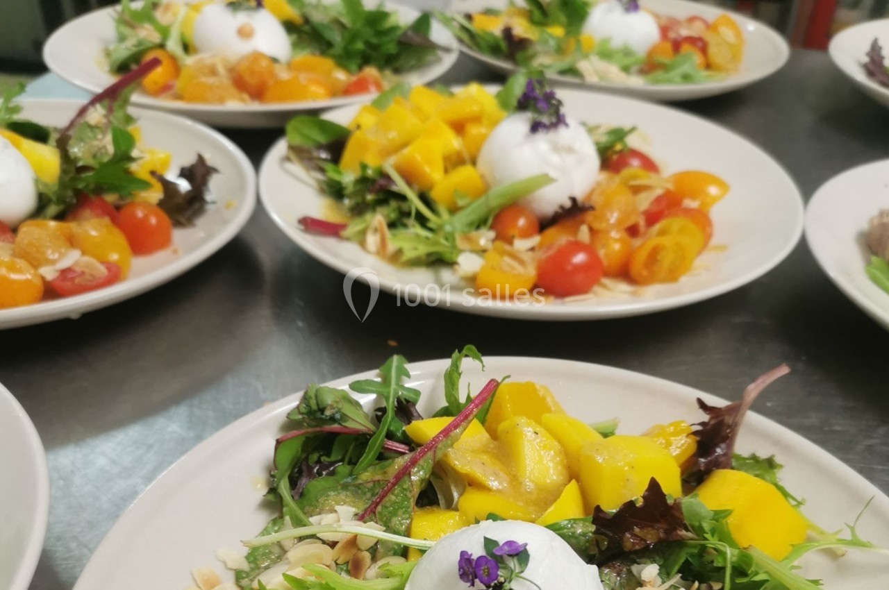Assiettes de salades colorées garnies de burrata, tomates cerises, mangues et feuilles de salade verte.