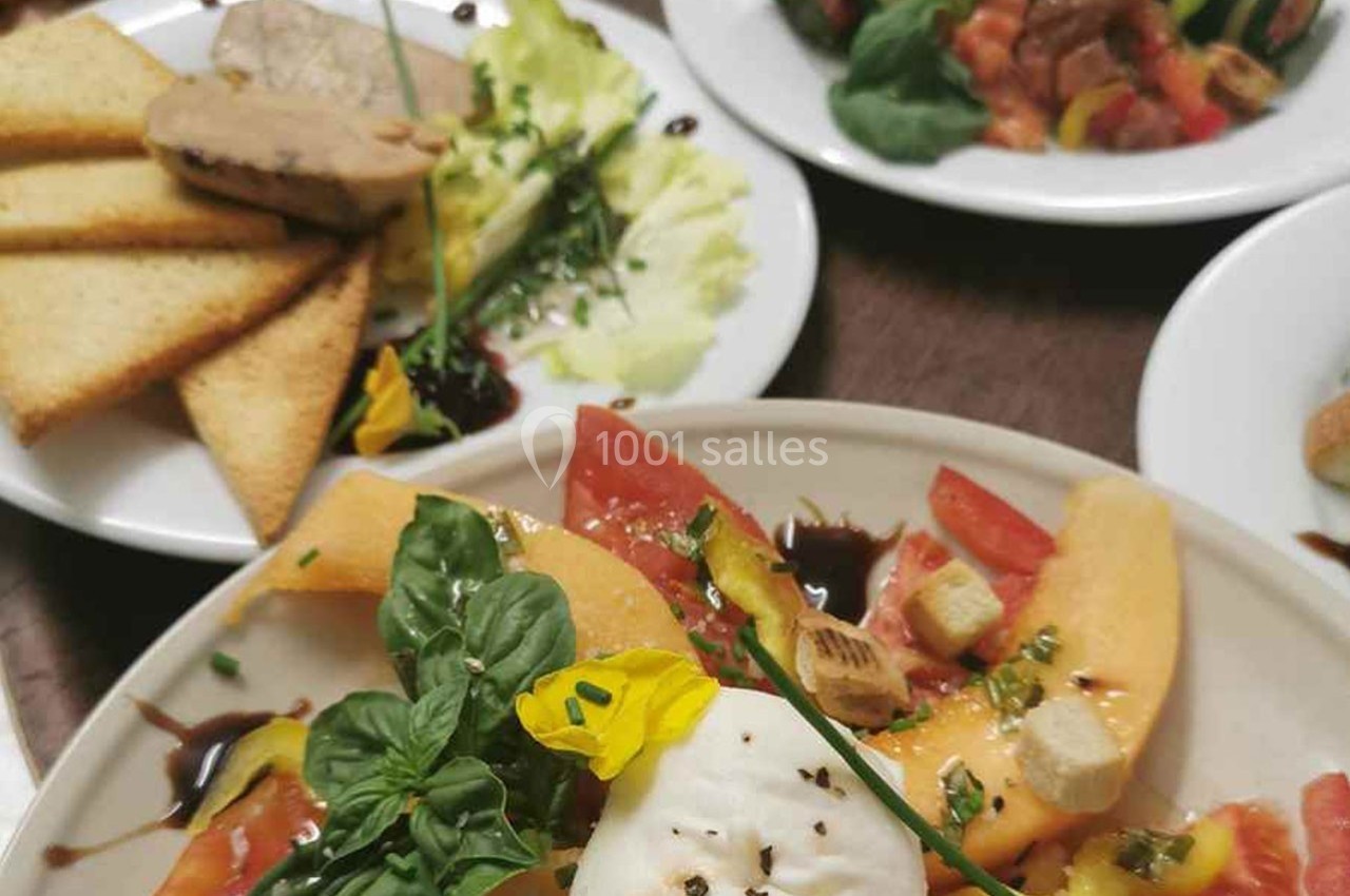 Assiette de salade composée avec melon, tomate, mozzarella, basilic et fleurs comestibles, accompagnée de toasts et foie…