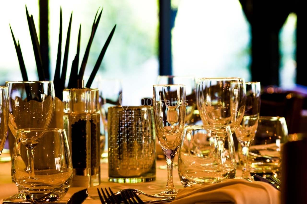 Table dressée avec des verres en cristal, une décoration végétale et un éclairage naturel en arrière-plan.