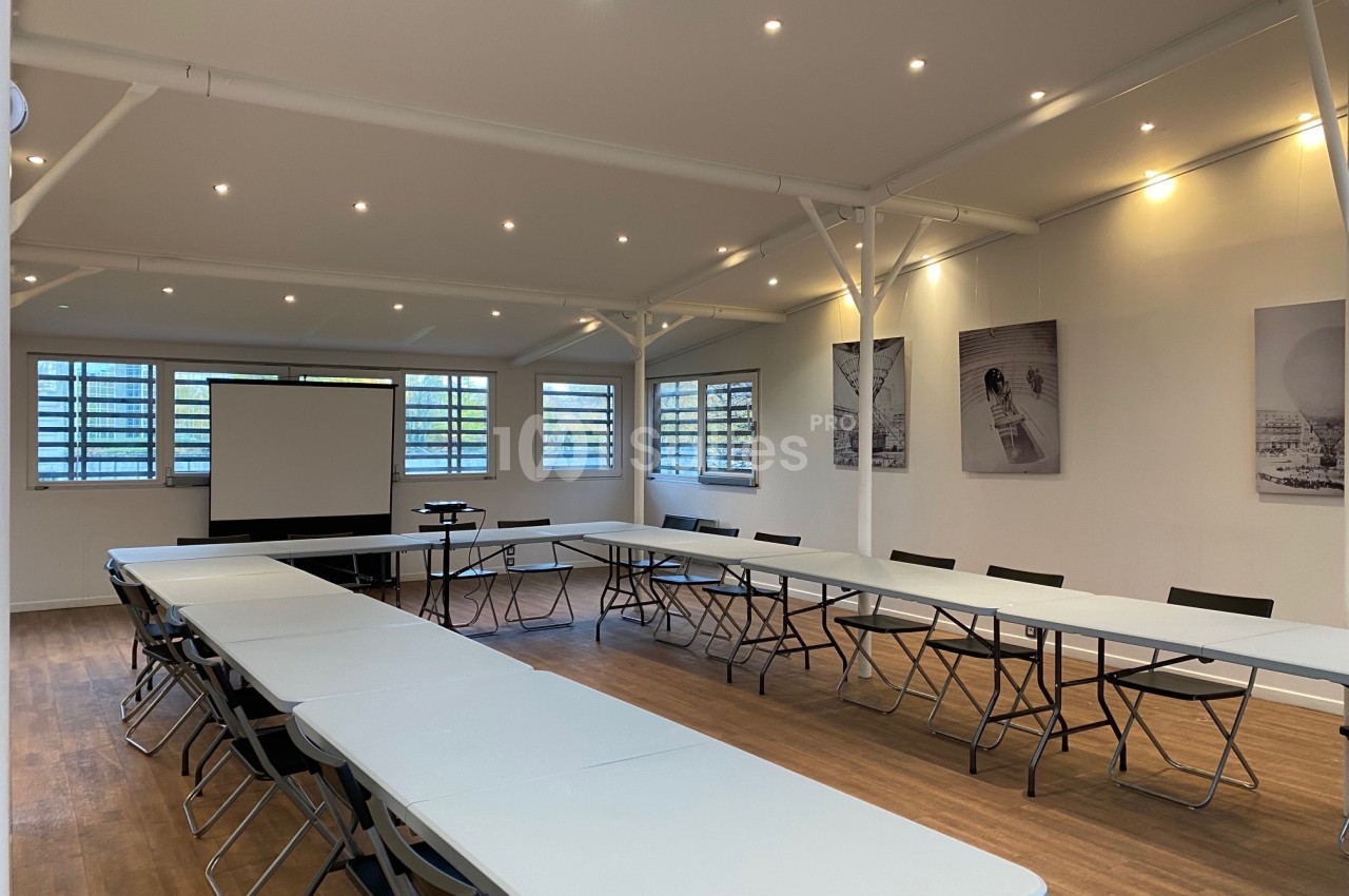 Salle de réunion lumineuse avec tables disposées en U, chaises noires, projecteur et tableaux accrochés aux murs.