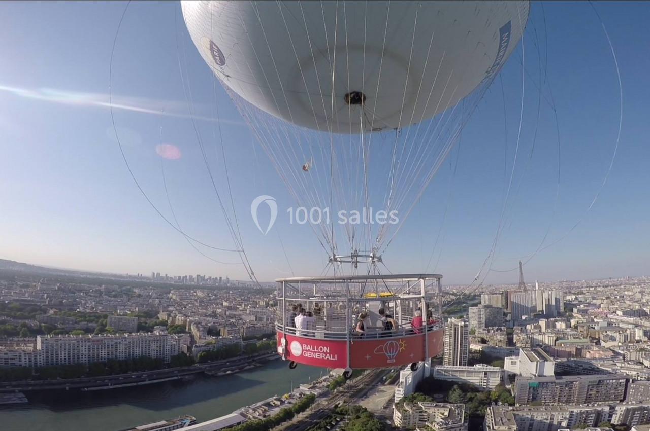 Montgolfière avec nacelle transportant des passagers survolant une ville avec une rivière et des bâtiments en arrière-plan.