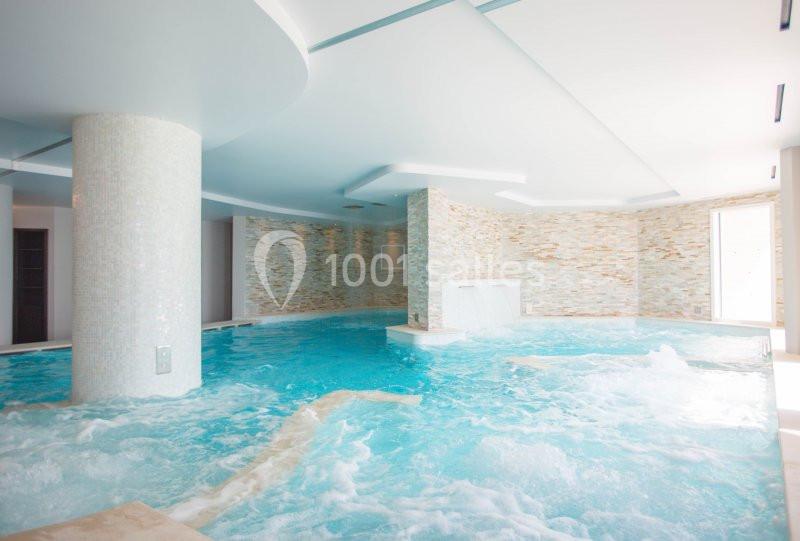 Piscine intérieure avec jets d'eau et murs en pierre claire, éclairée par une lumière naturelle.