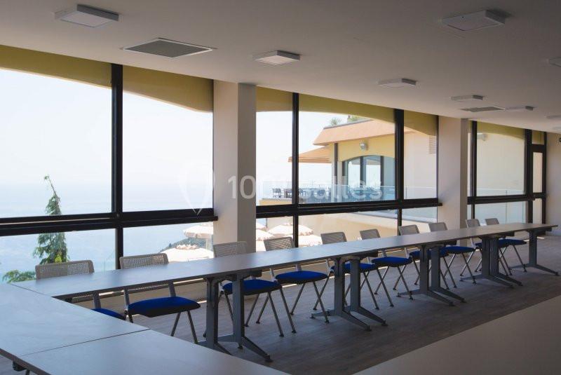 Salle de réunion lumineuse avec de grandes baies vitrées offrant une vue sur une terrasse et un paysage extérieur.