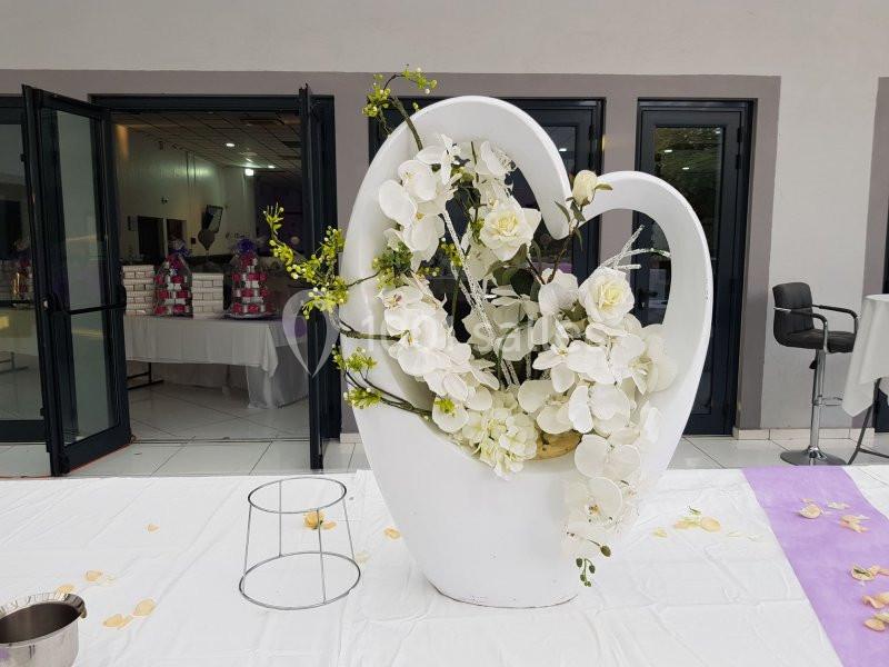 Arrangement floral blanc en forme de cœur, composé de roses et d'orchidées, placé sur une nappe blanche devant des portes…