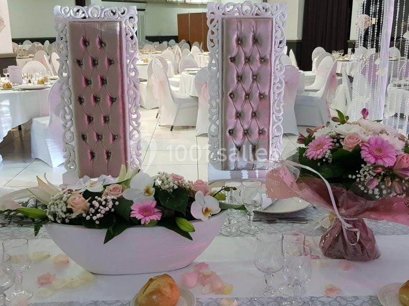 Salle de réception décorée avec des chaises ornées, une table fleurie et une vaisselle élégante.