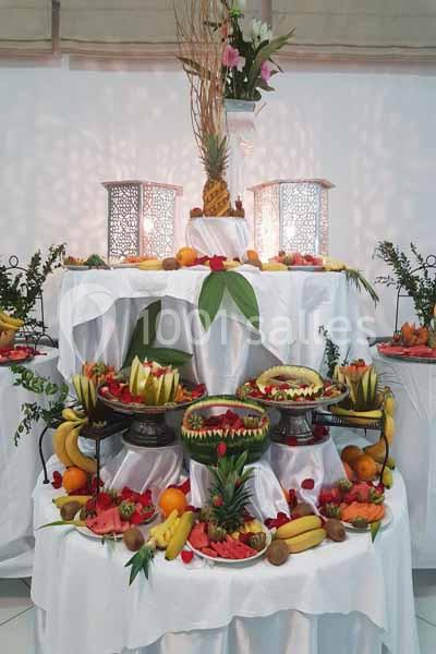 Présentation de fruits variés disposés artistiquement sur des plateaux et nappes blanches, avec des décorations végétales.