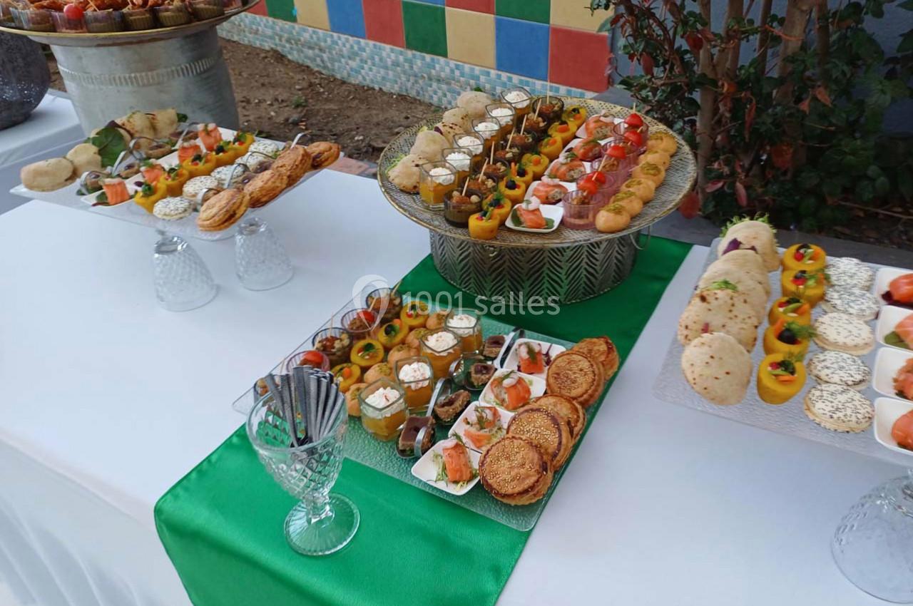 Buffet de hors-d'œuvre variés disposés sur une table blanche avec une nappe verte, en extérieur près d'un mur coloré.