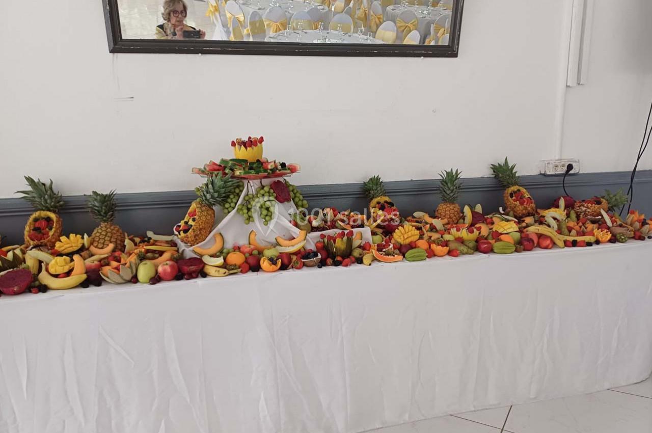 Buffet décoratif composé de fruits variés disposés sur une longue table blanche, avec des sculptures de fruits.