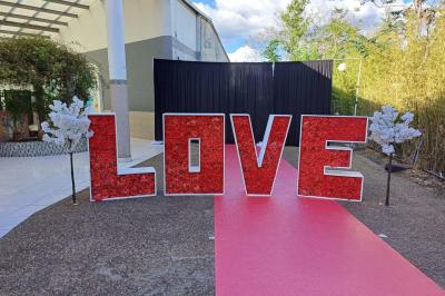 Lettres rouges formant le mot ’LOVE’ sur un tapis rouge, entourées de petites décorations blanches, en extérieur.