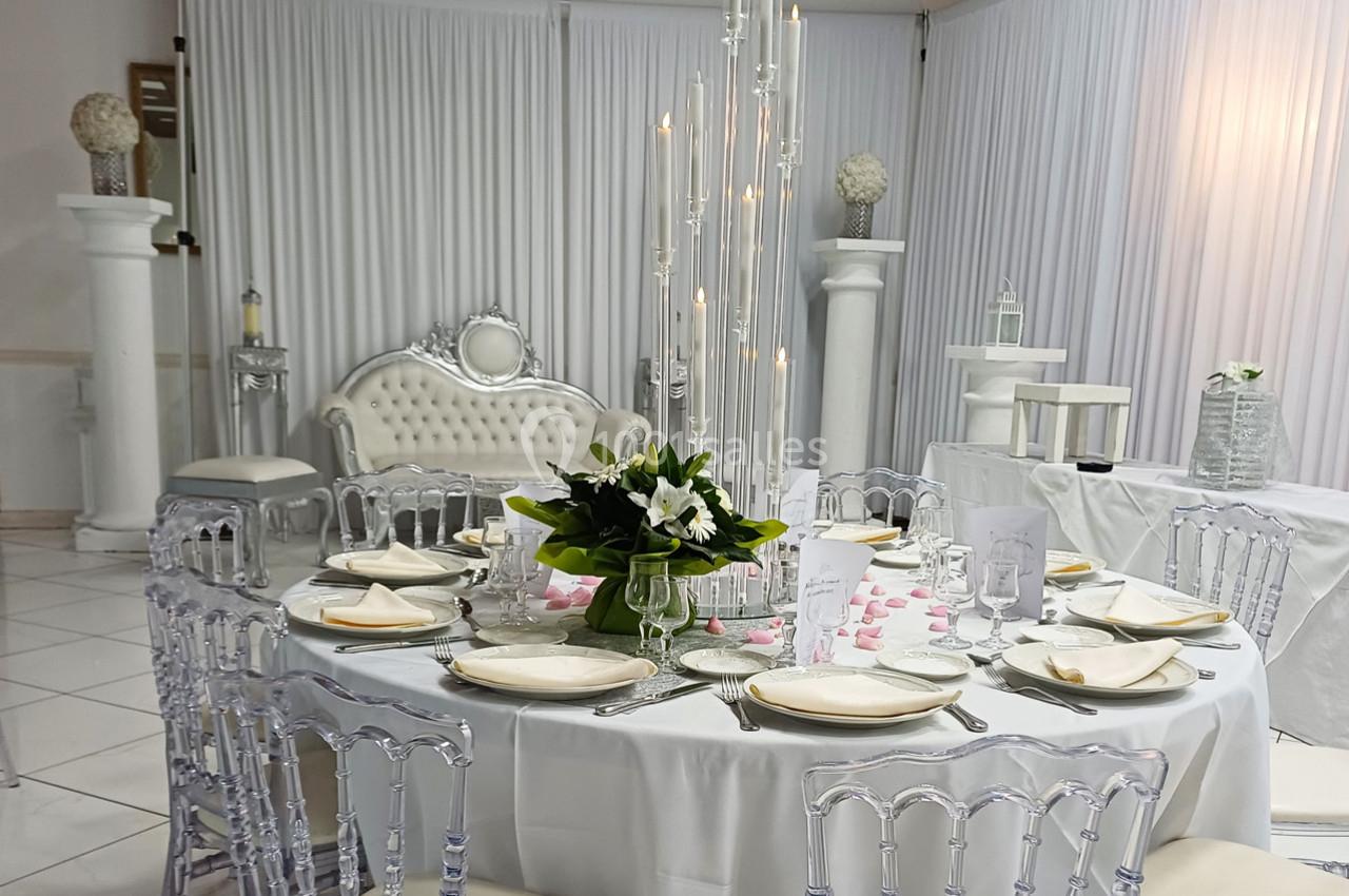 Salle de réception décorée avec une table ronde élégante, des chaises transparentes et un centre de table floral.